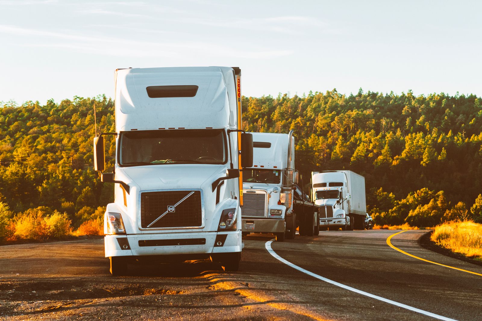 Semi trucks hauling freight on a highway at sunset
